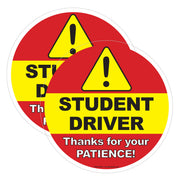 Two round stickers with yellow triangles and text about a student driver on a red background.